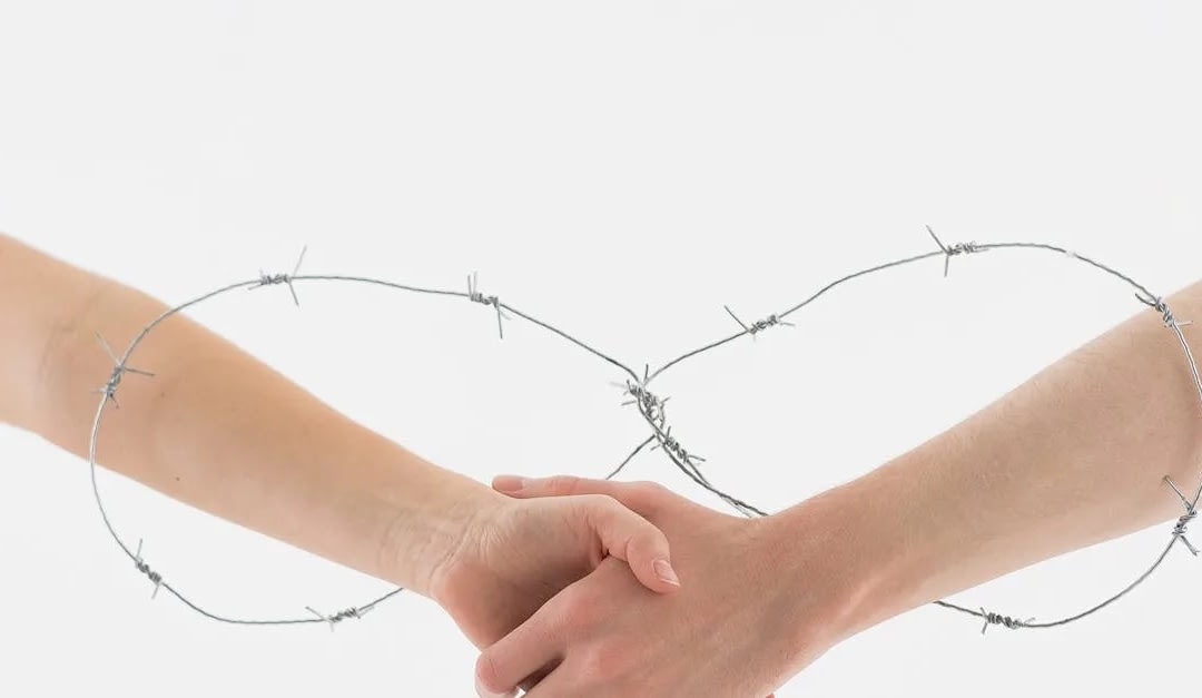 Two hands clasped in a handshake framed by barbed wire forming an infinity loop, symbolizing barrier-breaking unity.