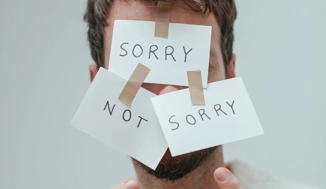 Man with white cards taped to his face reading 'SORRY' and 'NOT SORRY'.