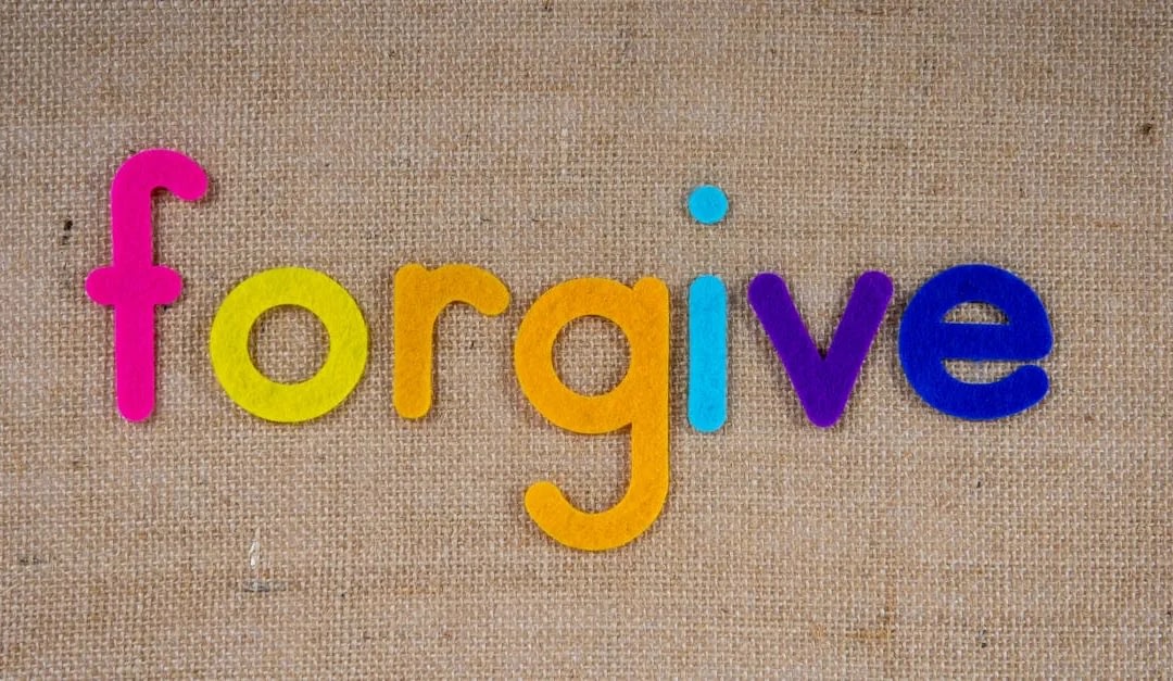 Colorful foam letters spell 'forgive' on a textured burlap background, rainbow colors from pink to blue.