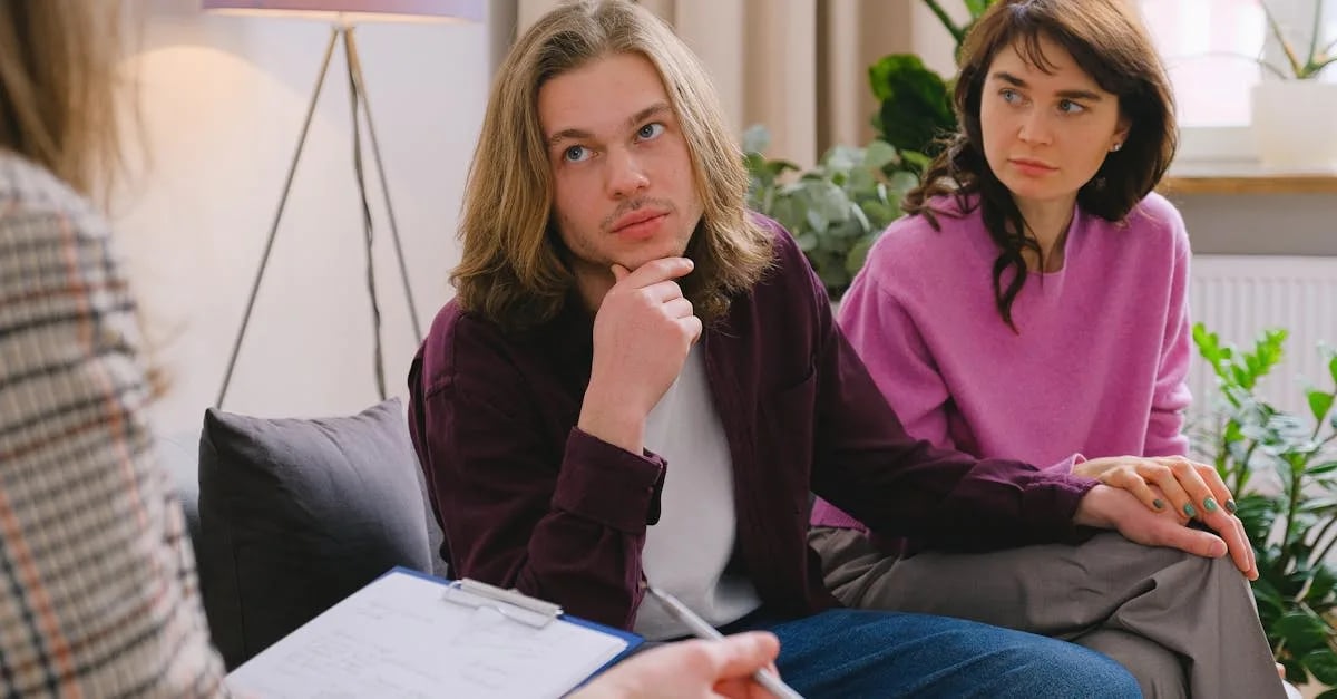 downloaded-image Couple in a therapy session sitting on a sofa; the man rests his chin thoughtfully while the woman looks on.