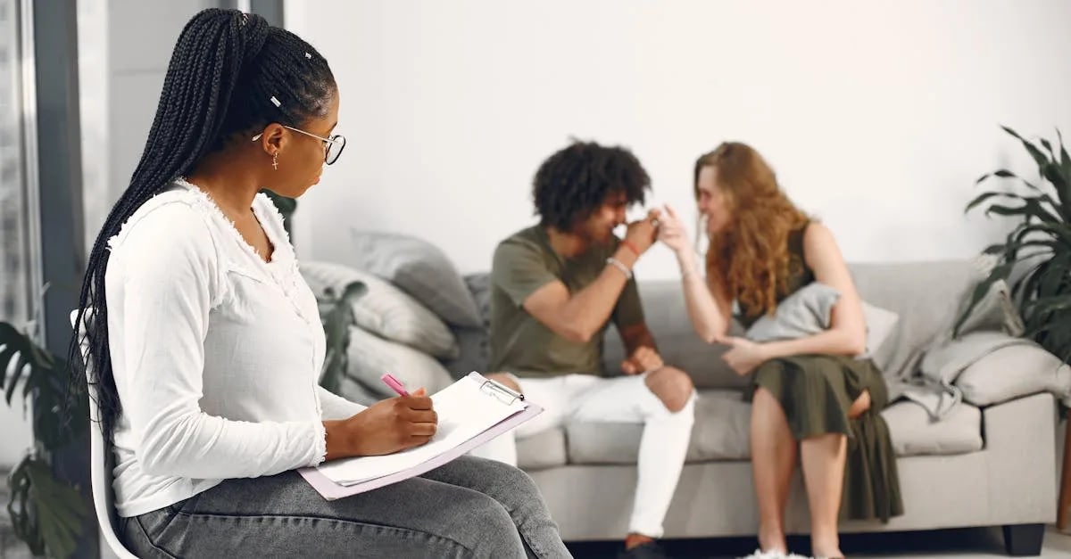 downloaded-image Therapist with clipboard taking notes while a couple on a sofa talk and laugh together in a bright living room.