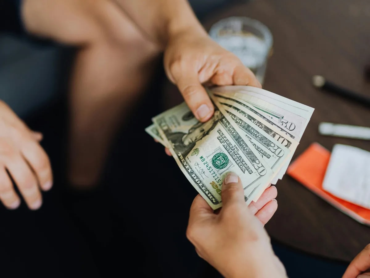 Blog July 21 (1) Hands reaching a fan of U.S. dollar bills, close up on cash.