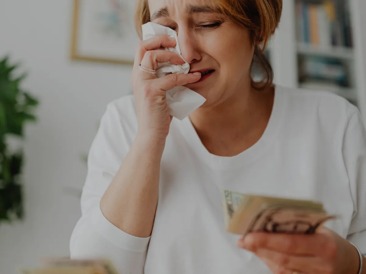 Blog July 21 (2) A woman holding her money while crying, seemingly experiencing financial abuse.