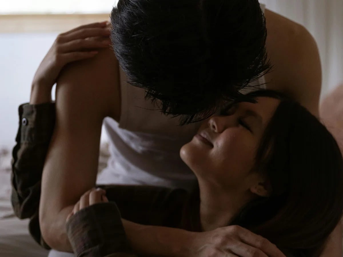 emotional-intimacy-vs-emotional-safety-2 Couple embracing in bed, sharing a kiss with the woman's face tilted up and a gentle smile.