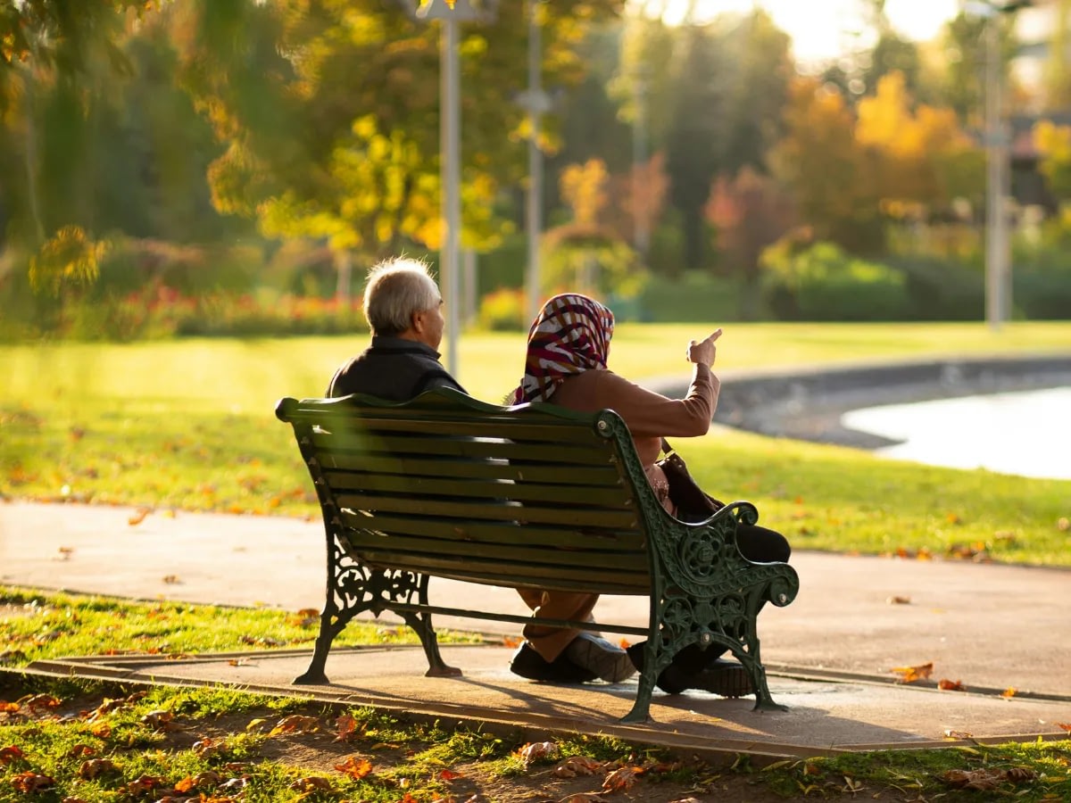 understanding-gray-divorce-1 An old couple sitting on a bench in the park at Autumn. The woman is pointing at something and the man seems to be looking at it as well.