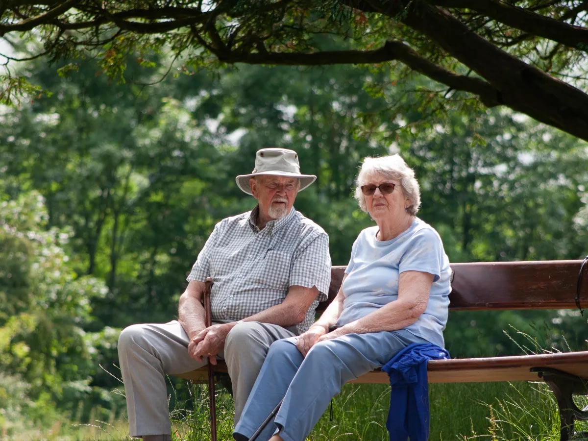 understanding-gray-divorce-2 An old couple talking while sitting on a bench in the park. The man is looking at the woman and the woman is looking at the camera.