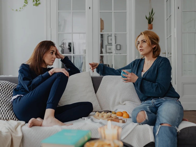 Two women talking while sitting in a couch.