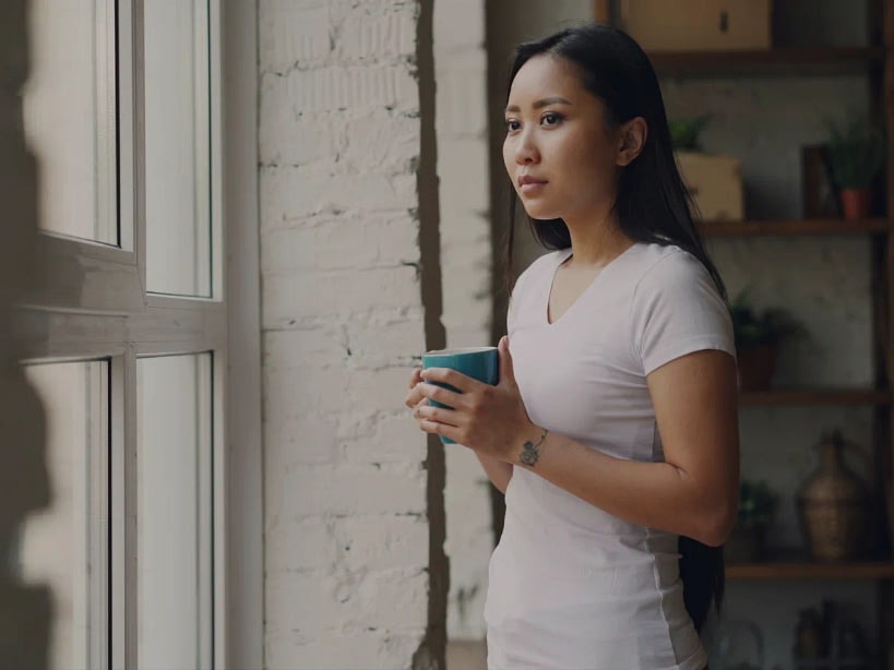 Adult sitting quietly by a window, reflecting with a cup of coffee.